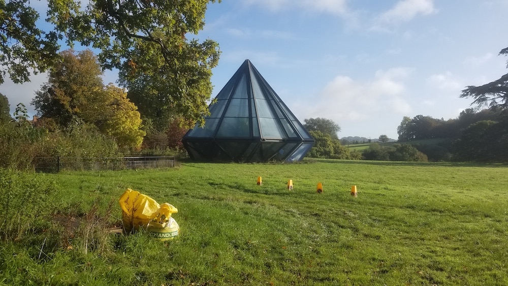 A glass pyramid-shaped building stands on a grassy field.