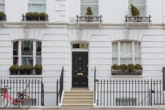 Elegant white London townhouse with black front door, iron railings, and potted plants, representing trusted house sitting London